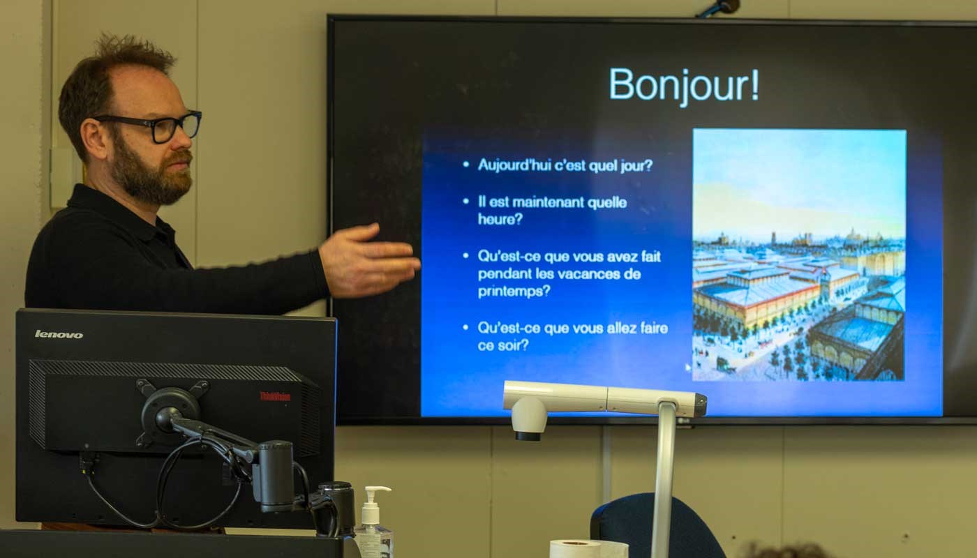Professor stands before a video monitor in a French class at UMass Lowell