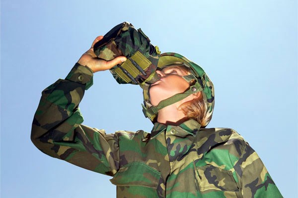A soldier in camouflage drinking from a canteen.
