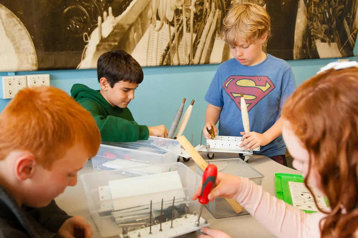 Four children work on a craft at a table with supplies on it