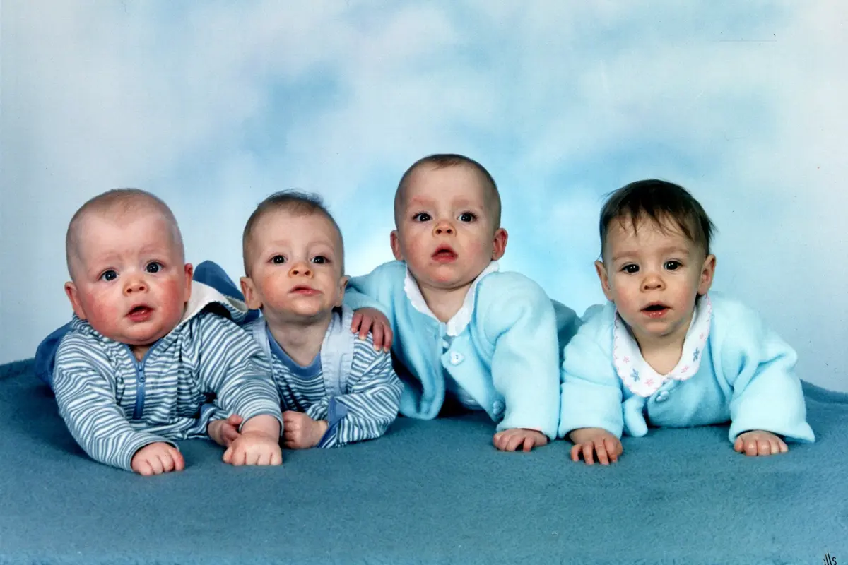 Quadruplet babies pose for a photo against a blue backdrop.