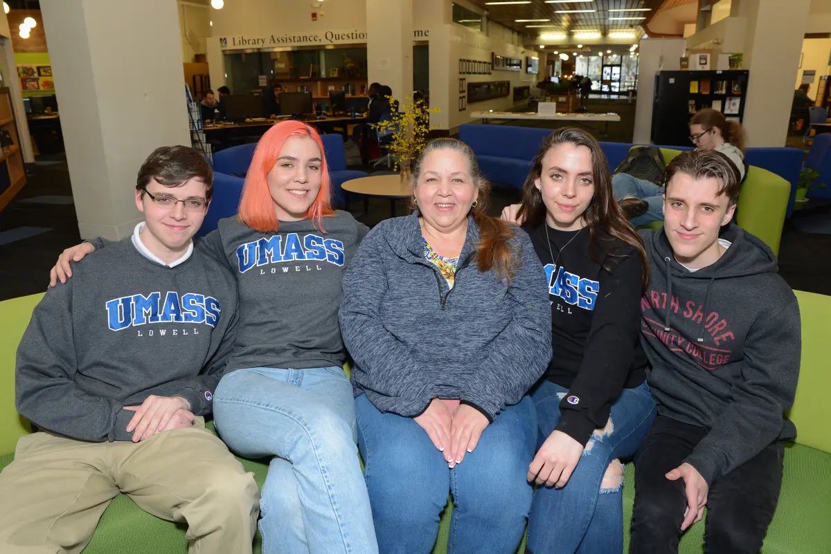 Two young men and two young women pose for a photo with their mom while seated on a couch in a lobby.