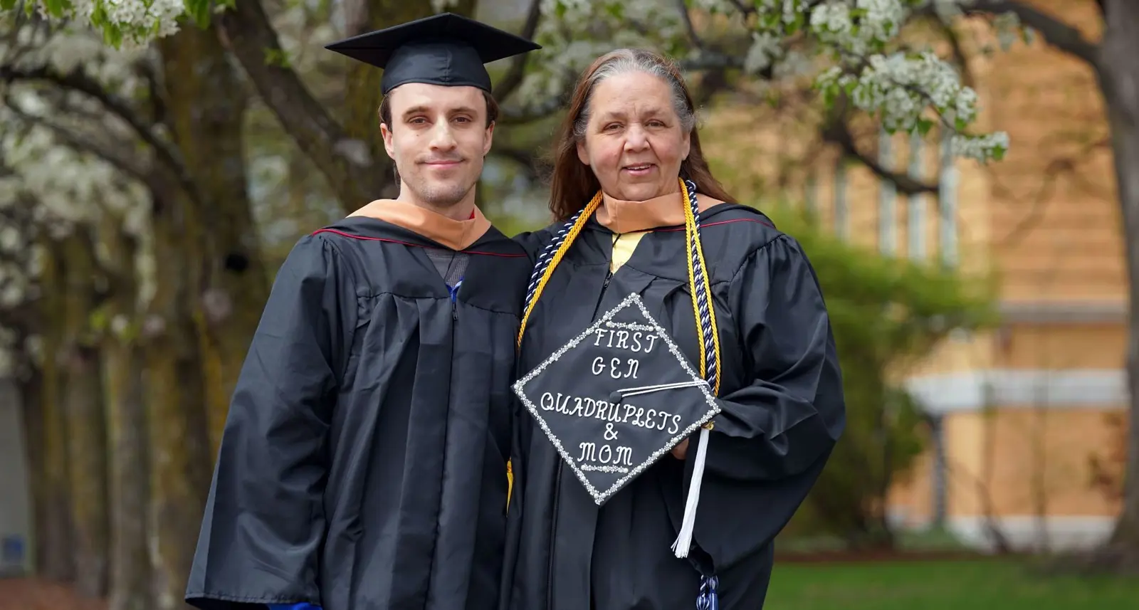 Bryce and mom Maureen Whitcomb in their graduation regalia holding cap with Frist Gen Quadruplets & Mom on it