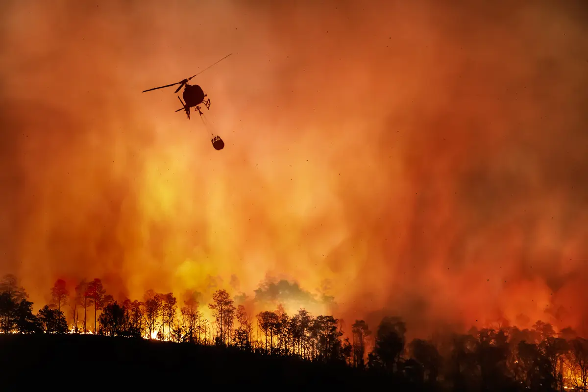 A helicopter hovers over a raging wildfire to drop fire suppressant chemicals.