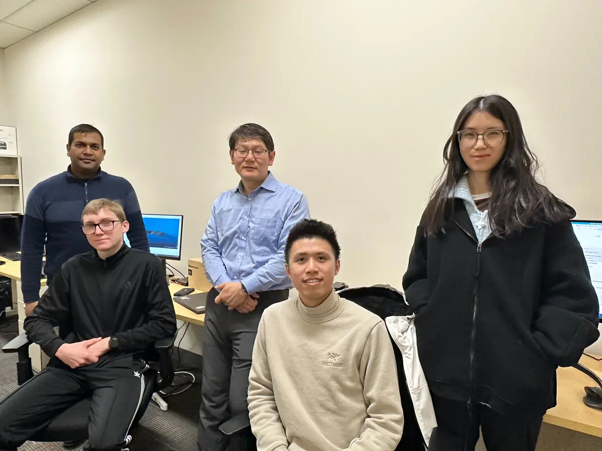 Five people stand and sit in Professor Yuanchang Xie's lab of computer stations and cameras