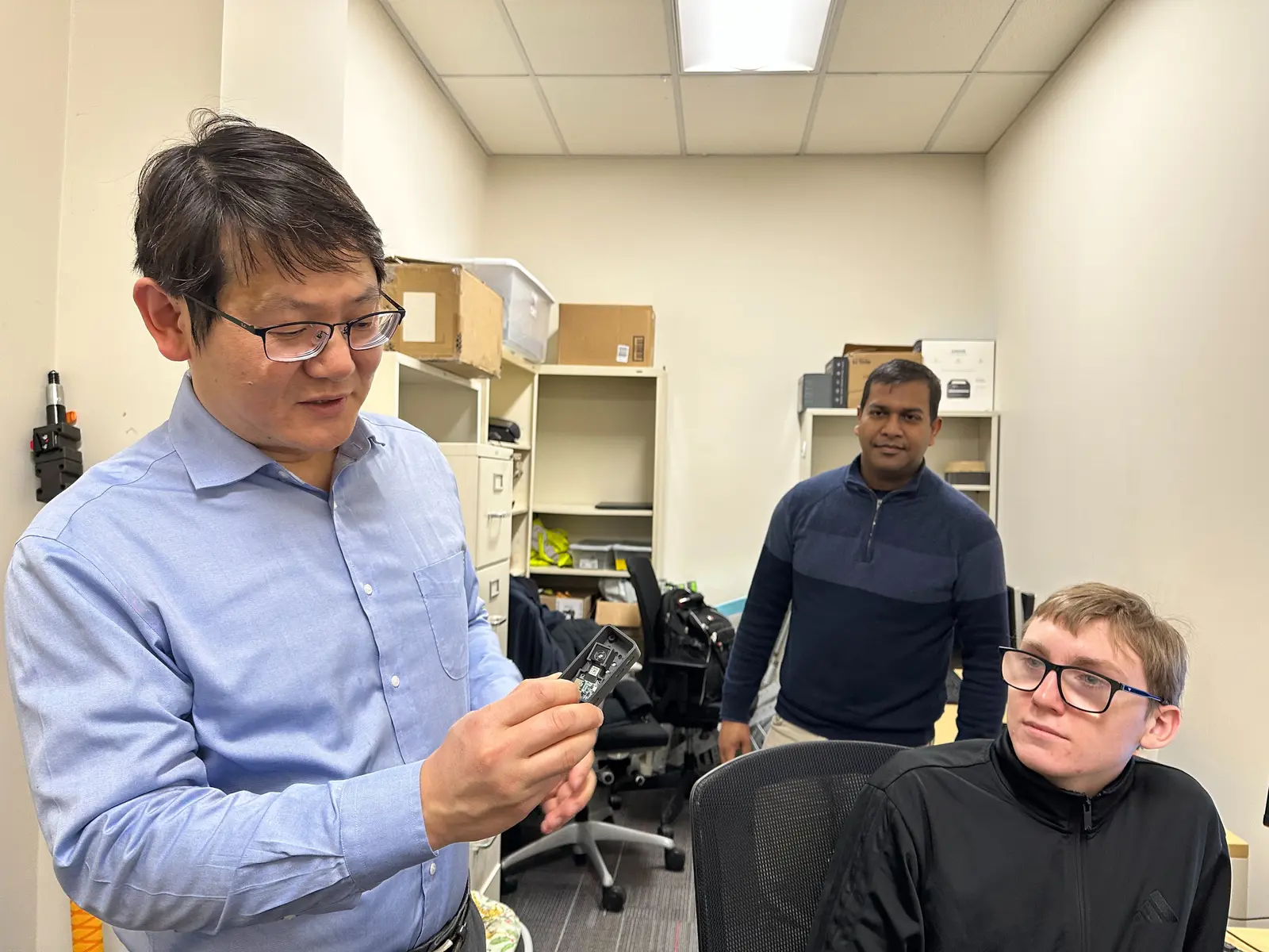 Professor Yuanchang Xie shows off a camera as two young men watch