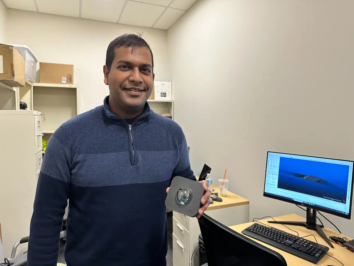 A smiling postdoc, Zubin Bhuyan, holds up a camera for counting vehicles and pedestrians