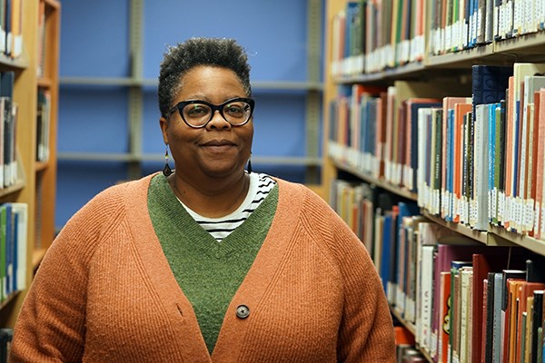 A woman with short dark hair and glasses poses for a photo in a library
