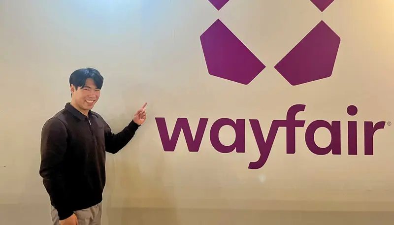 Zander Lai points to the Wayfair logo that is painted on a wall.