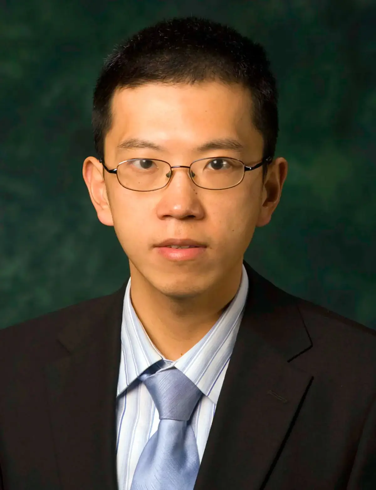 A posed headshot photo of a man with dark hair and glasses and wearing a suit.