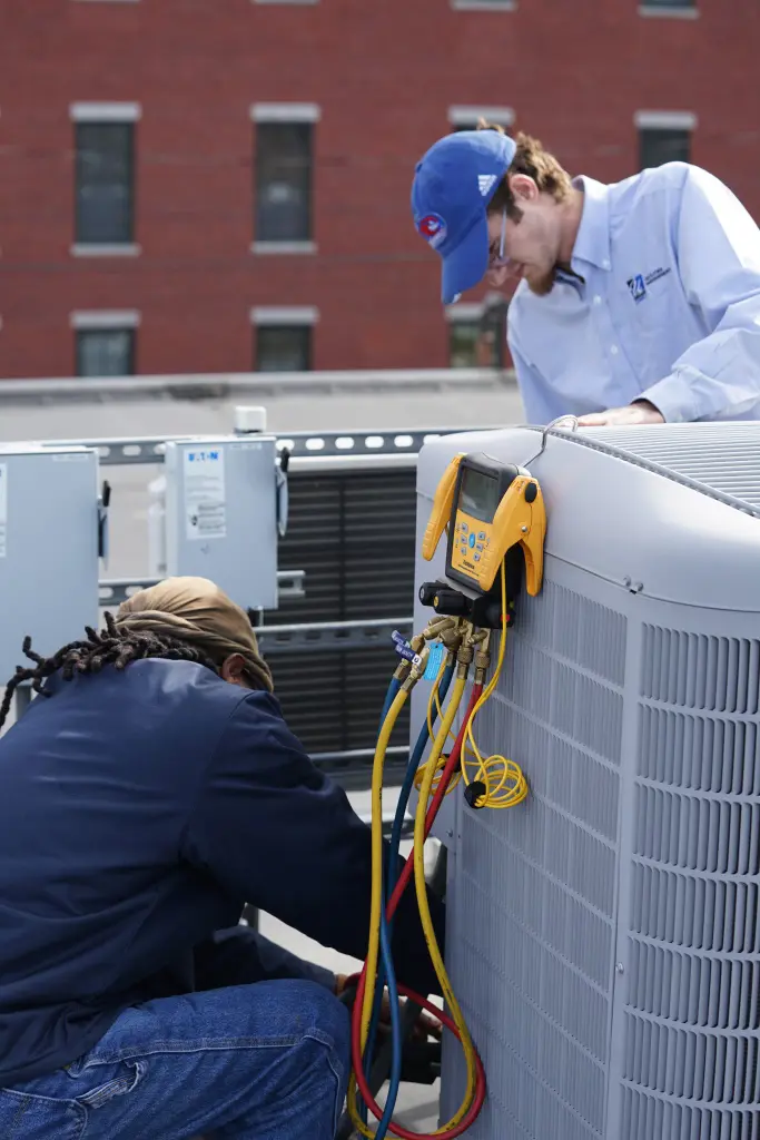 Two workers tending to air conditioning unit on a roof