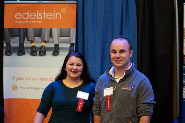 A woman and man pose for a photo together at a career fair booth