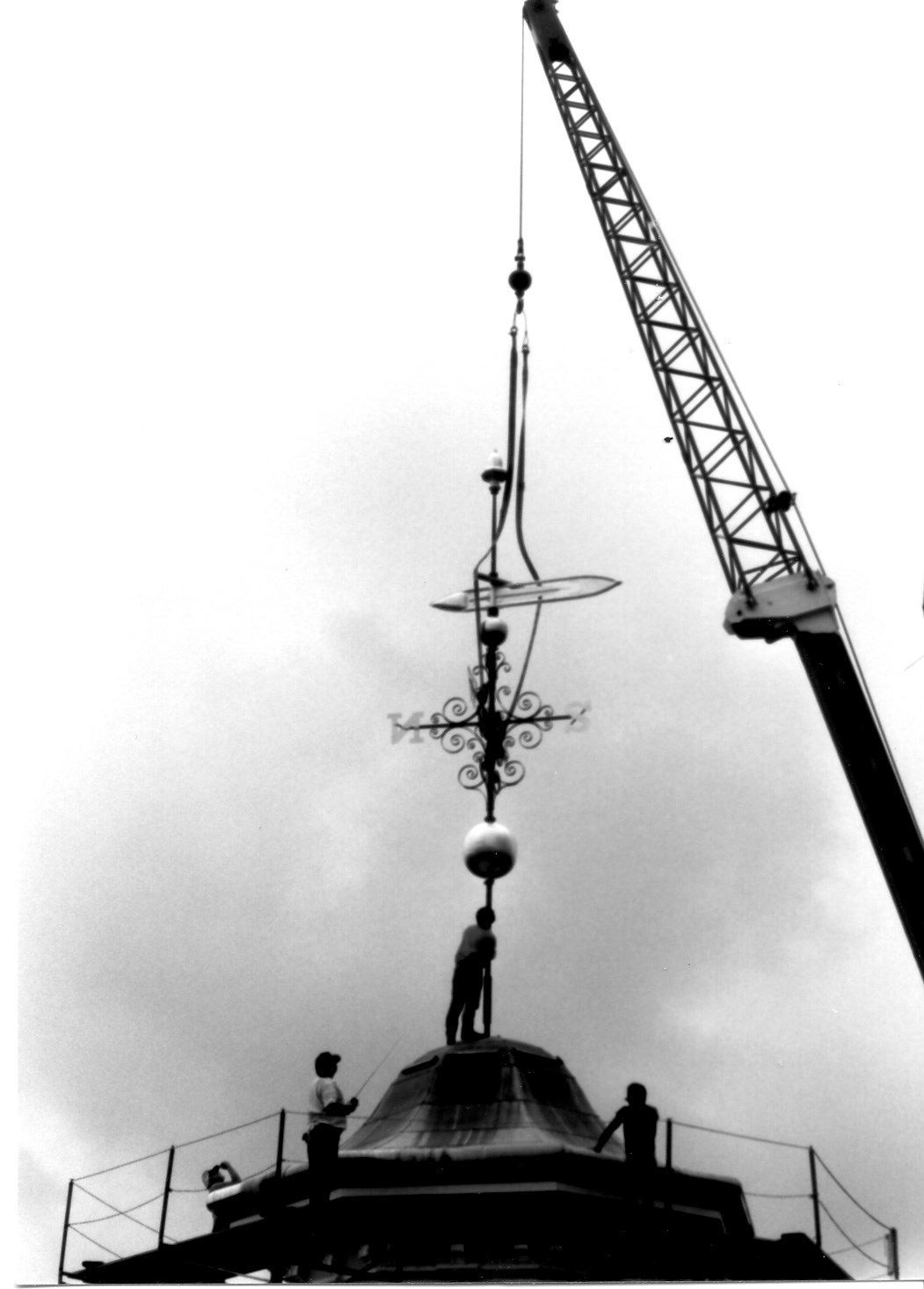 Crane and workers removing the top acorn weathervane of the Boott Mill clock tower