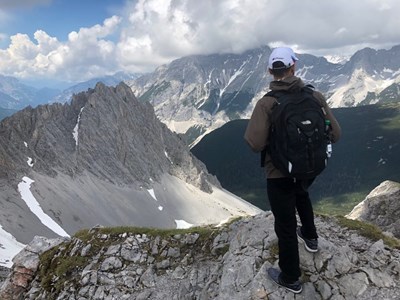 Student with backpack looking down at the mountain range from a summit in Innsbruck, Austria.