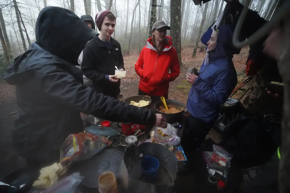 People serve themselves dinner from pots of food and talk to each other.  
