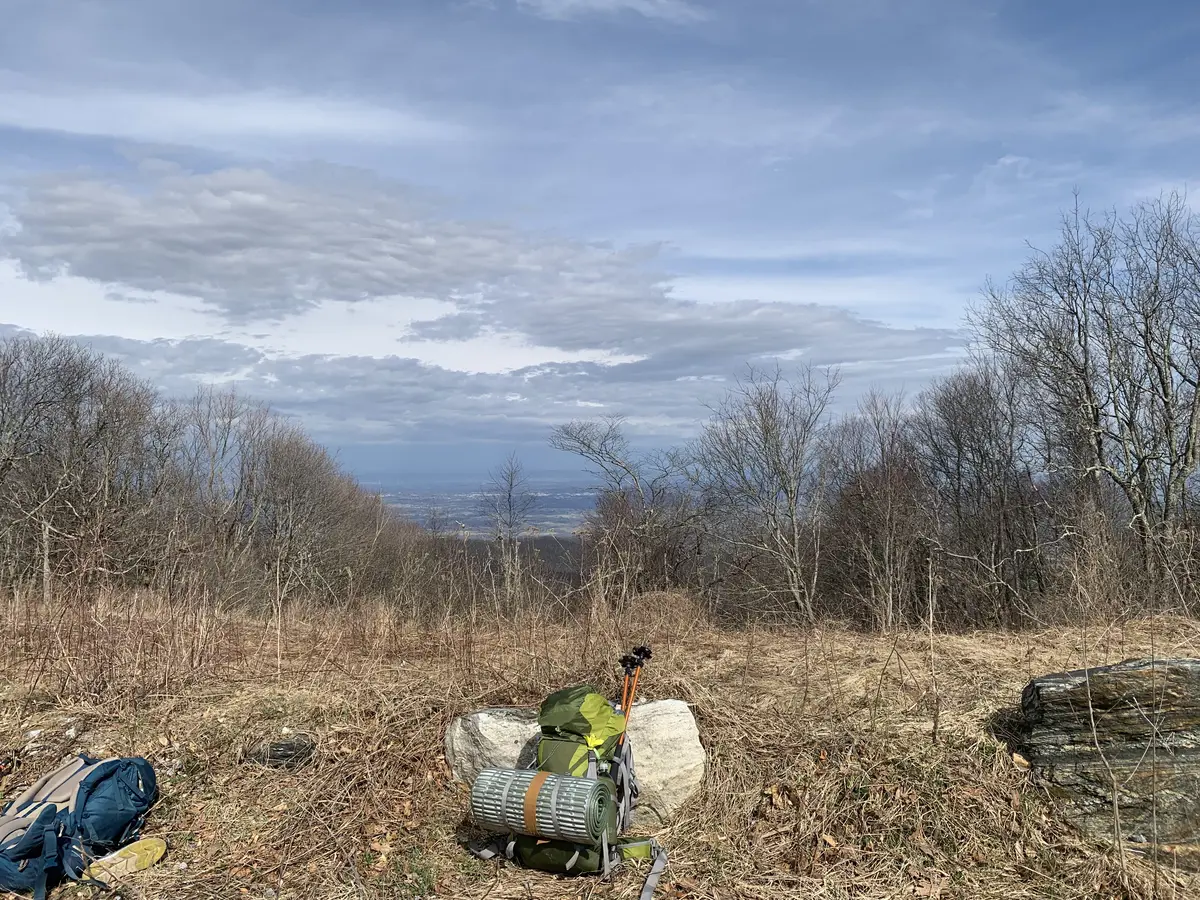A viewpoint from the top of a mountain with a backpack and trekking poles on the ground. 