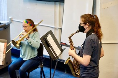 Two teenage girls play brass wind instruments in a classroom