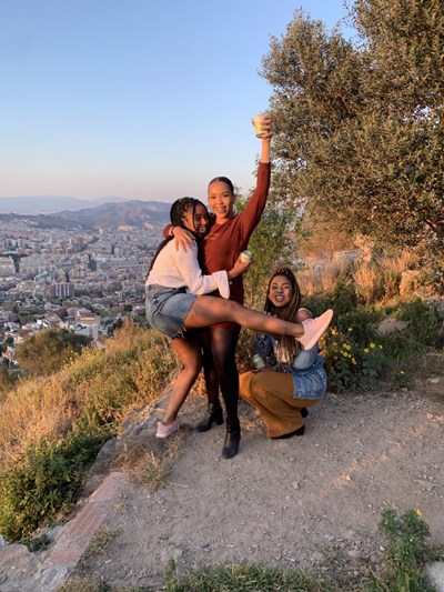 Luzmia Ligonde and two friends stand on a hill at sunset overlooking Barcelona, Spain