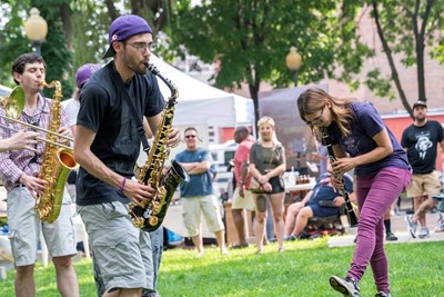 three band members play saxophones in an outdoor park