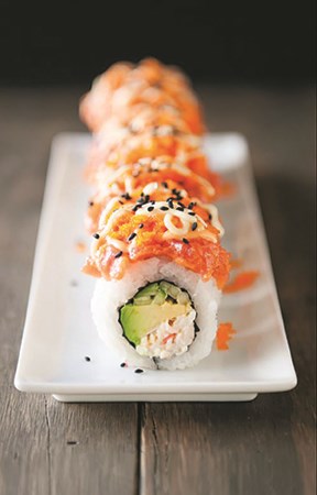 A sushi roll with crab and avocado sits on a plate in a row
