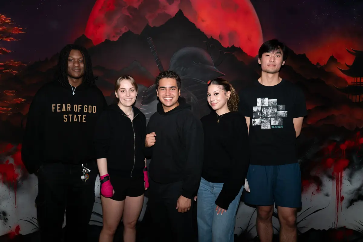 Three young men and two young women pose for a group photo at a boxing gym.