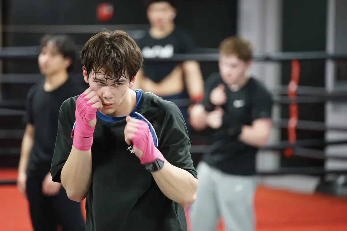 A college student with his hands wrapped in pink tape works out at a boxing gym.