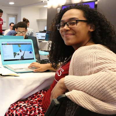 Young Black woman smiles over shoulder while working on laptop