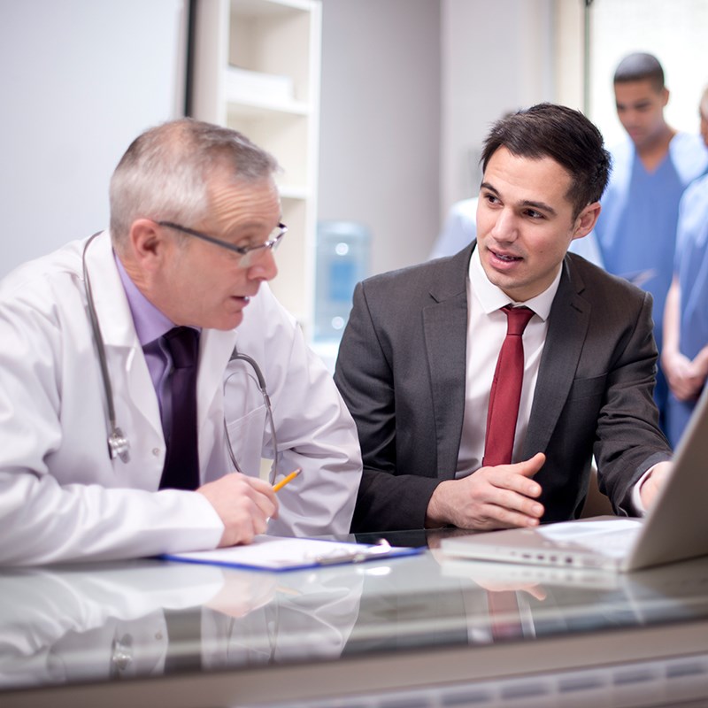 Male doctor speaks with young man in business suit looking at laptop
