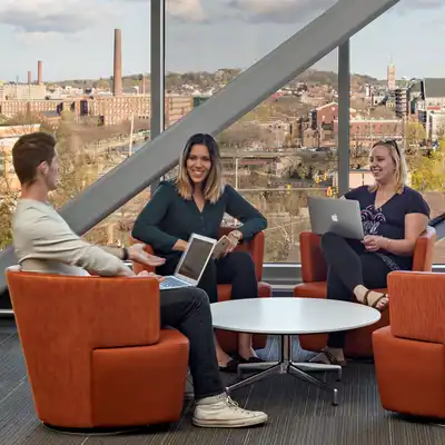 Three students with laptops sit together in a UMass Lowell business school room.