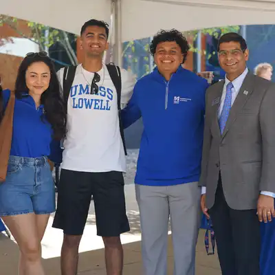 Three students wearing UMass Lowell shirts pose with a business professor.