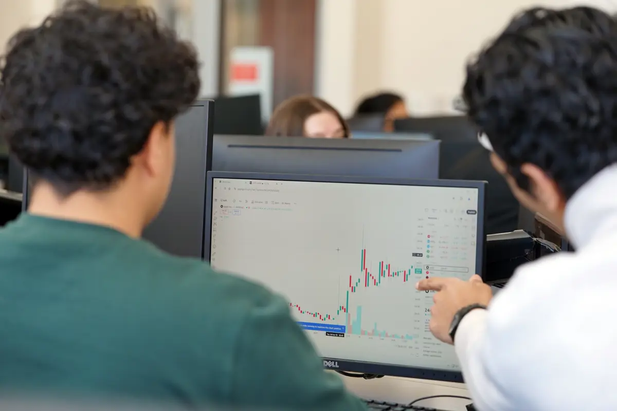 One person points at a graph on a computer screen while another looks on.