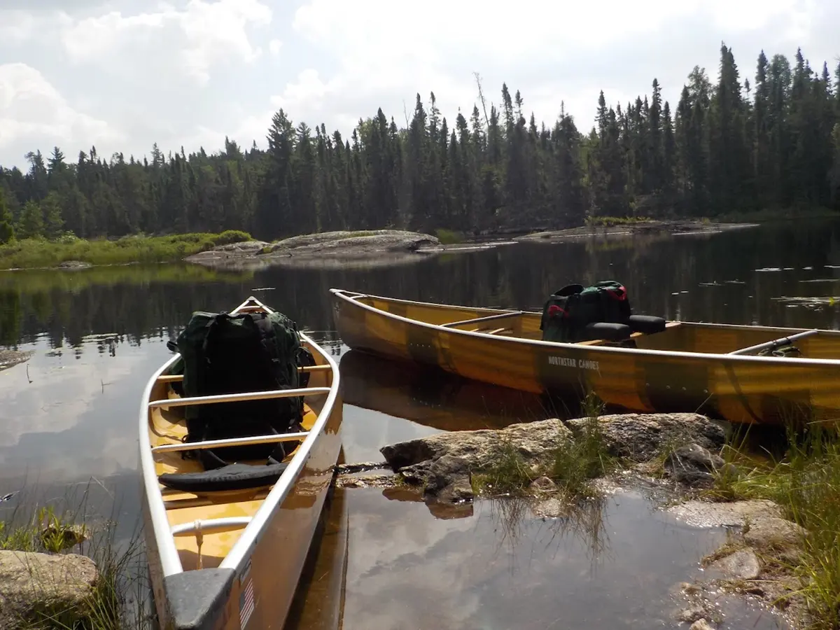 Two loaded canoes sit against a rocky shoreline.