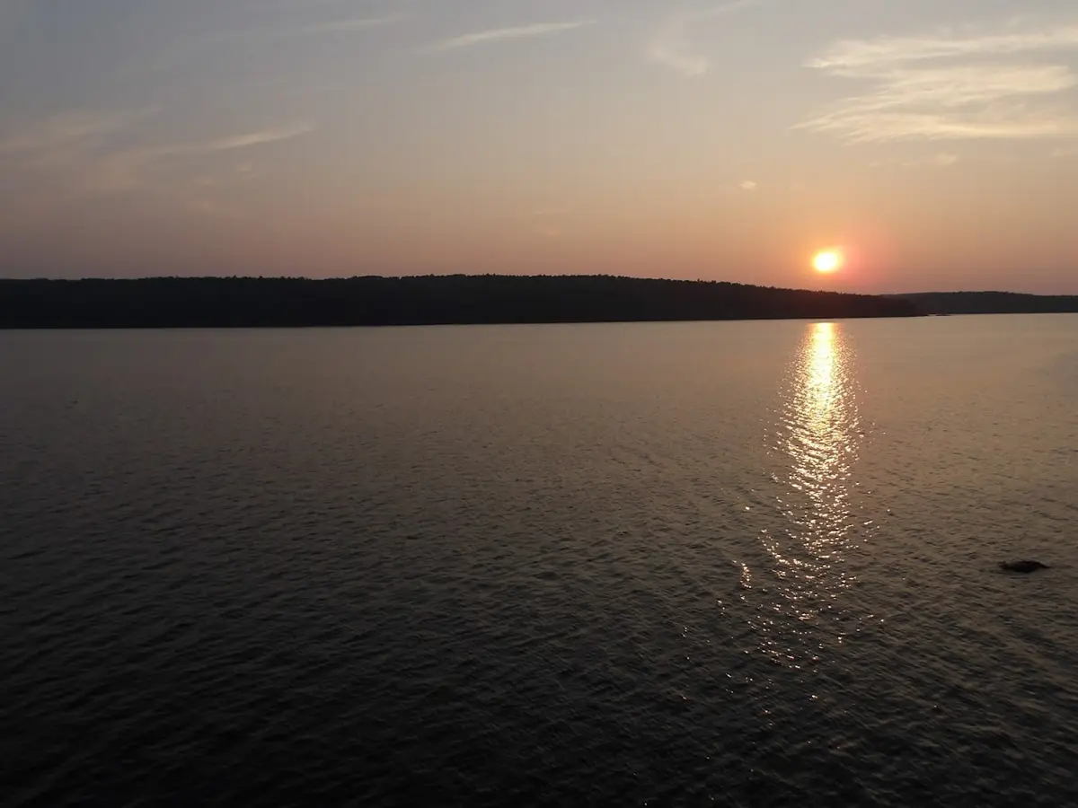 The glowing orange orb of the sun sits just above the far tree line and reflects on the water from a high view. 