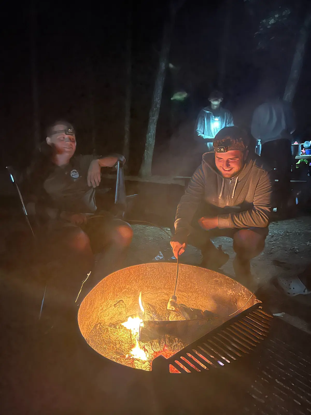 Two people roast marshmallows at a campfire.