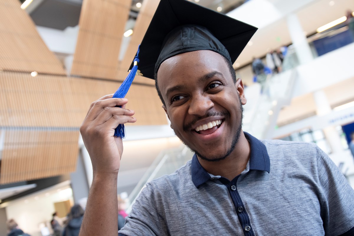 A male undergraduate student tries on his mortar board cap for graduation.