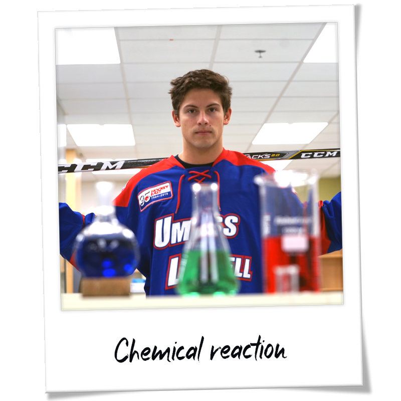 "Polaroid" shot of Charlie Levesque wearing his River Hawks hockey uniform holding a hockey stick in a chemistry lab - handwriting on frame reads "Chemical reaction" 