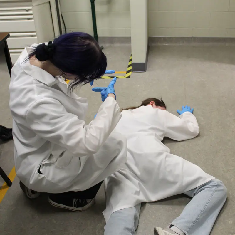 A forensic science student practices taking measurements of a person who is lying on the floor.