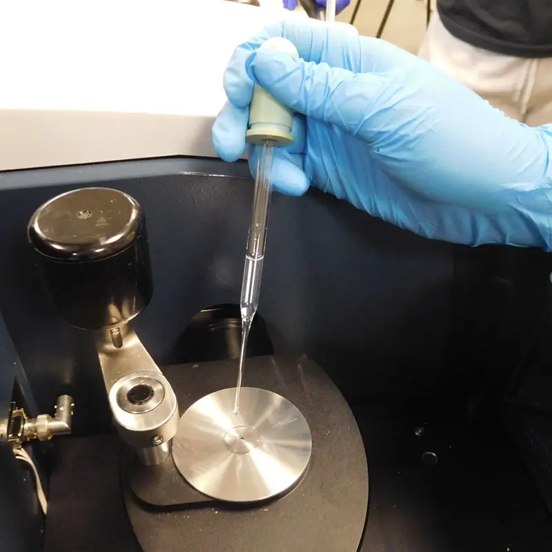 A gloved hand dispenses liquid through a pipette in a UMass Lowell chemistry lab.