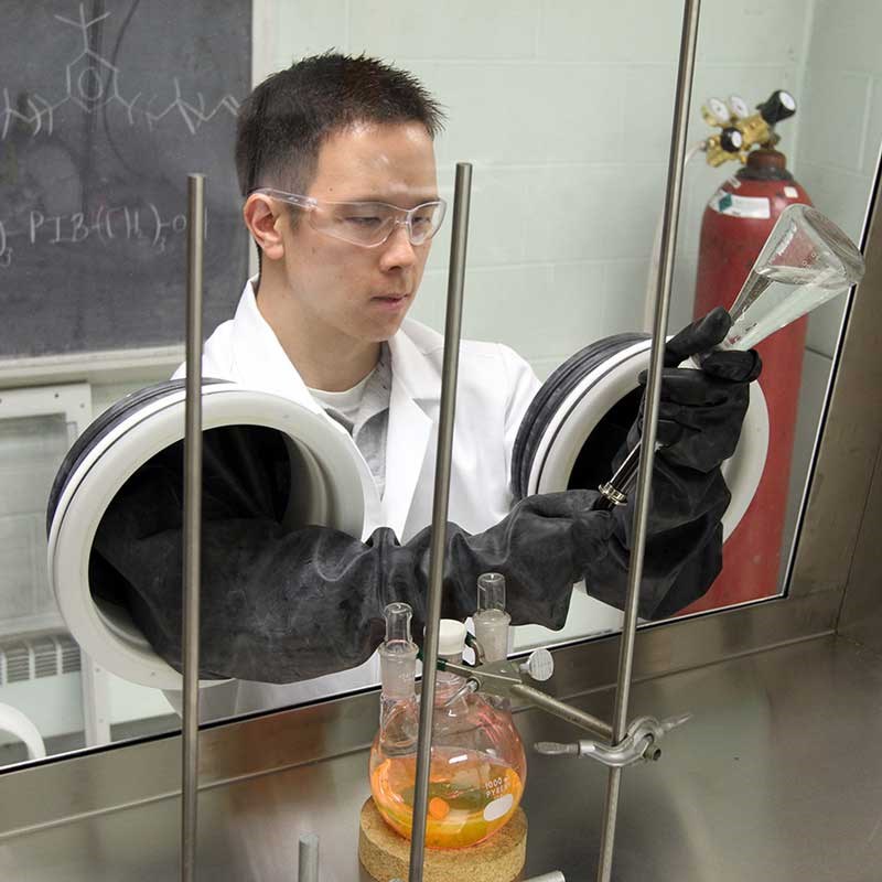 Chemistry research student wearing arm-length gloves and working with lab equipment