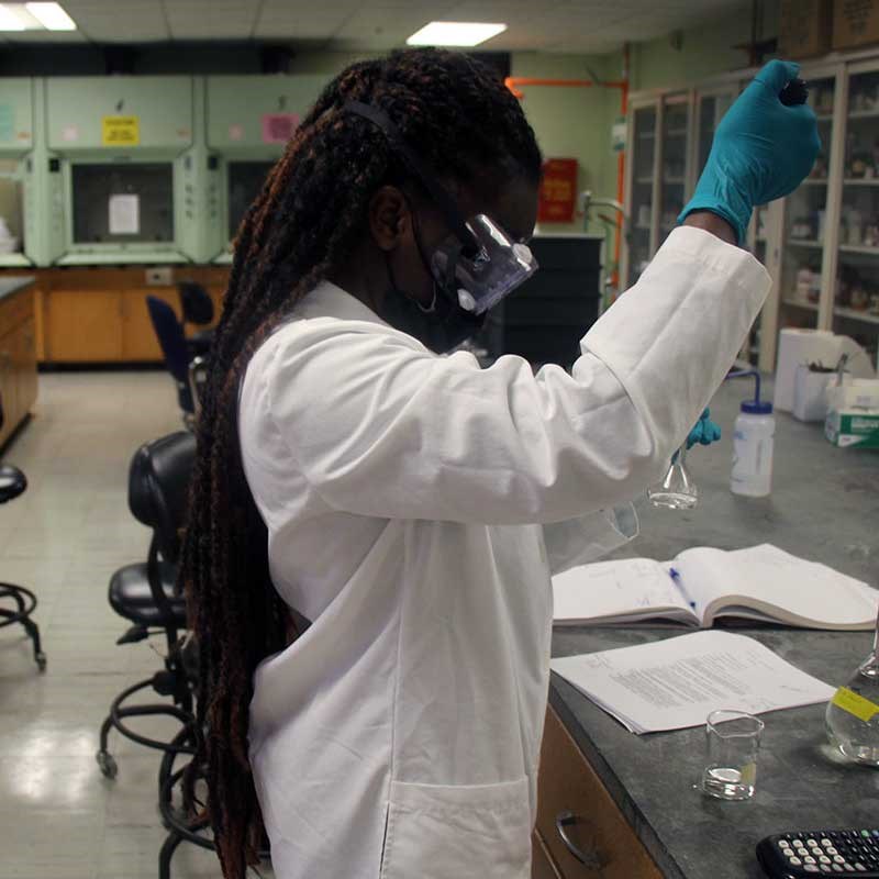 Chemistry student in lab coat works with equipment in a UMass Lowell lab