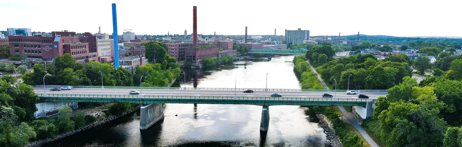 Cars driving over bridge over river with smokestacks and buildings in background