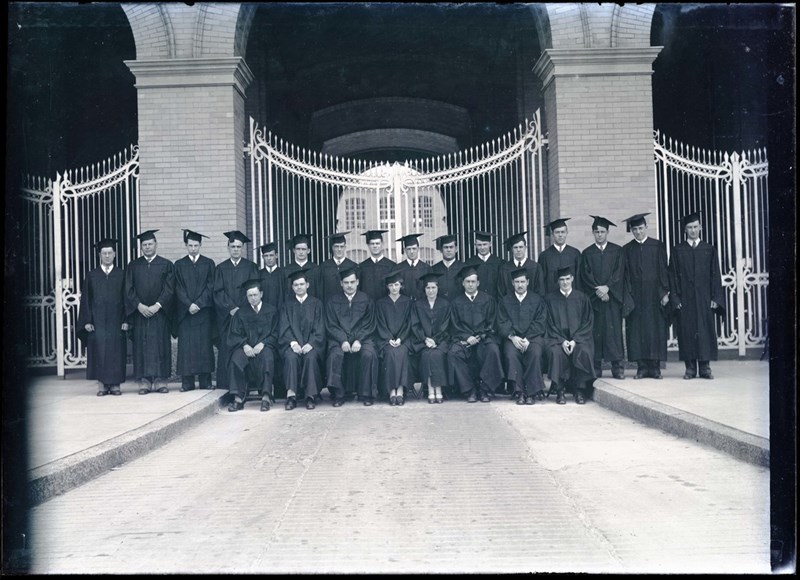 Graduates from the class of 1930 pose for a photo in caps and gowns outside the gates of Southwick Hall on North Campus