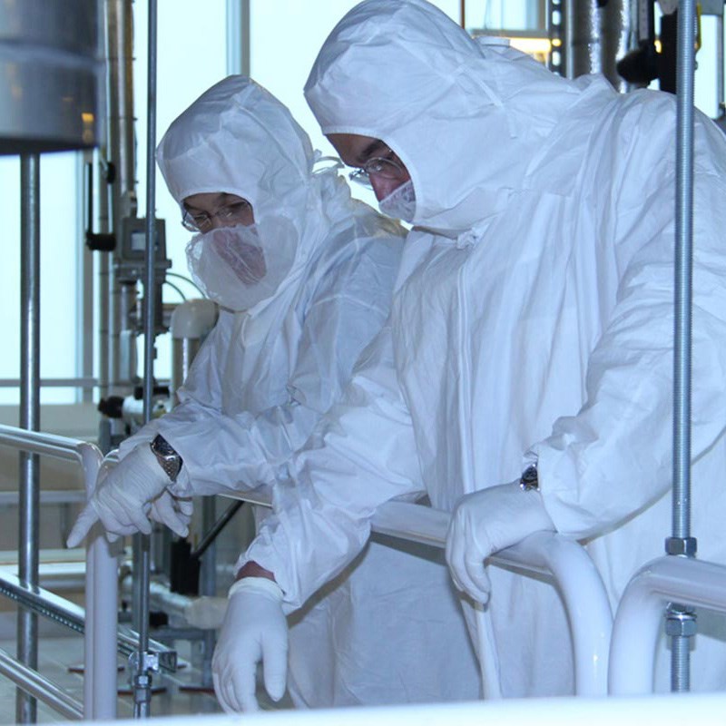 Two people wearing white suits head to toe working in clean room.