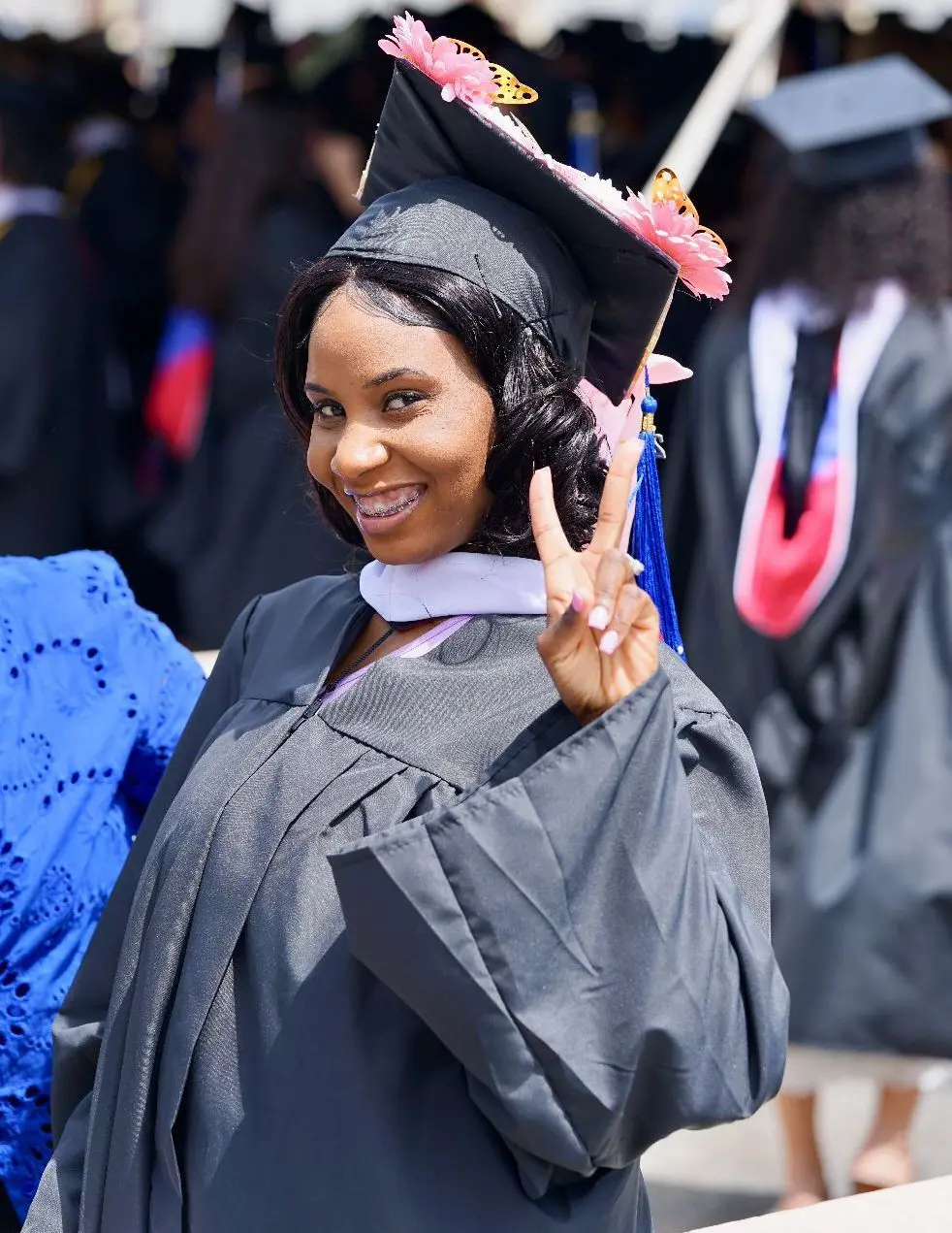 Young woman in cap and gown smiles and flashes peace sign