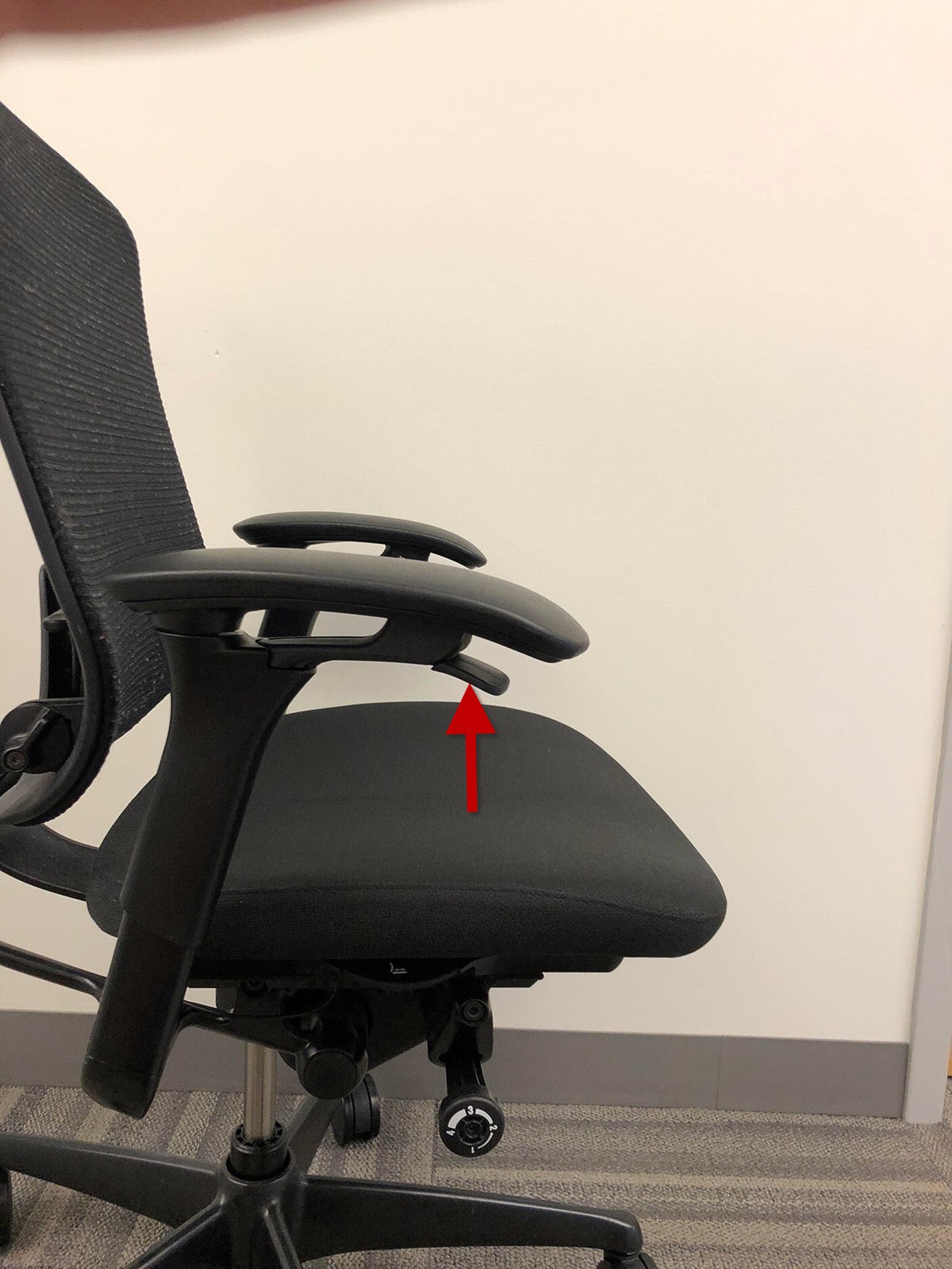 An empty contessa chair with an arrow pointing to the lever under the right armrest.