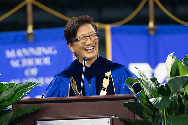 A woman with short hair and glasses smiles while speaking at a podium