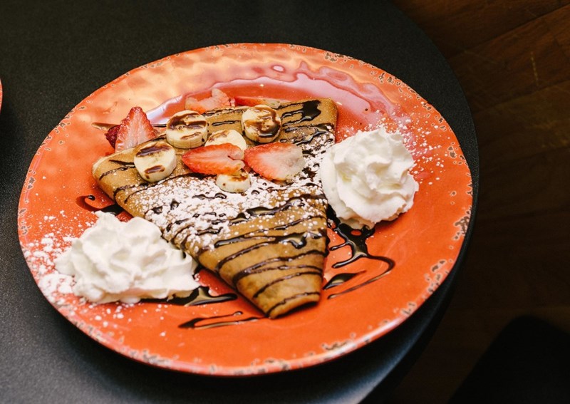 A crispy crepe on an orange plate drizzled with chocolate and topped with bananas, strawberries and whipped cream