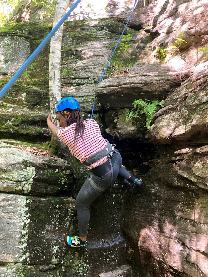 woman in a harness hangs on a rope while gripping a tree and rock climbing