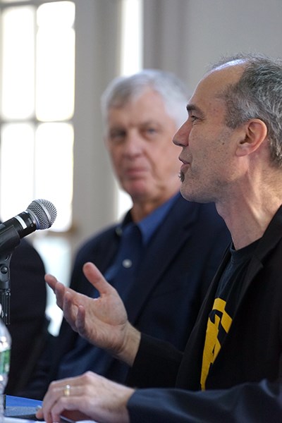 A man speaks into a microphone as another man looks on