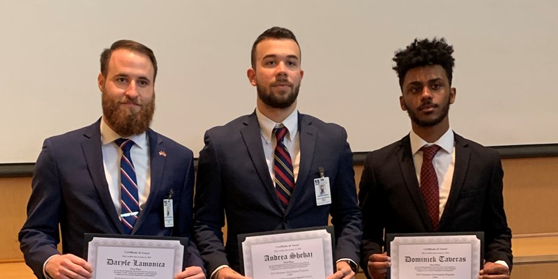 Daryle Lamonica stands with two other students, all in suits, holding certificates for completing a summer enrichment program