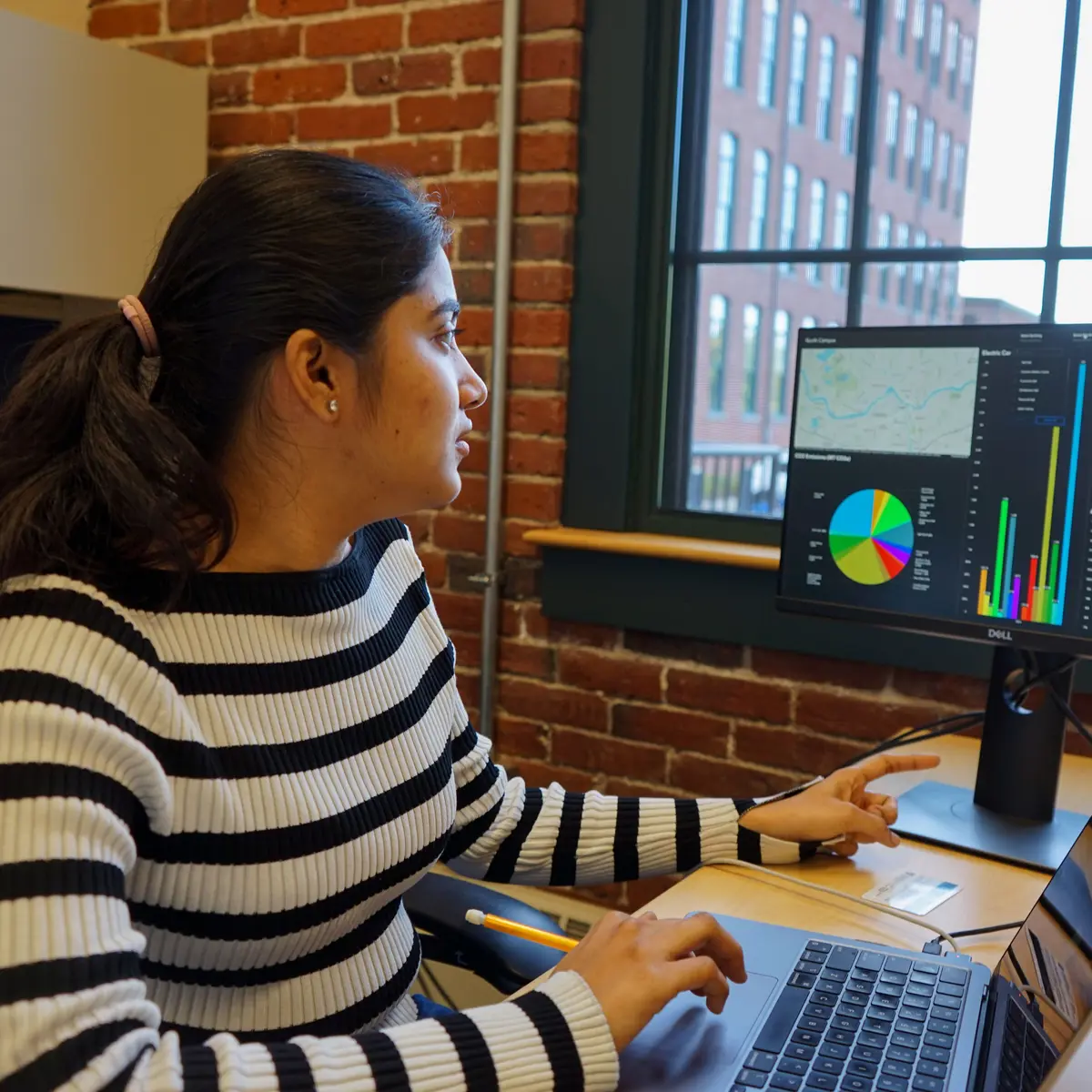 Student using a laptop points at data on a screen.
